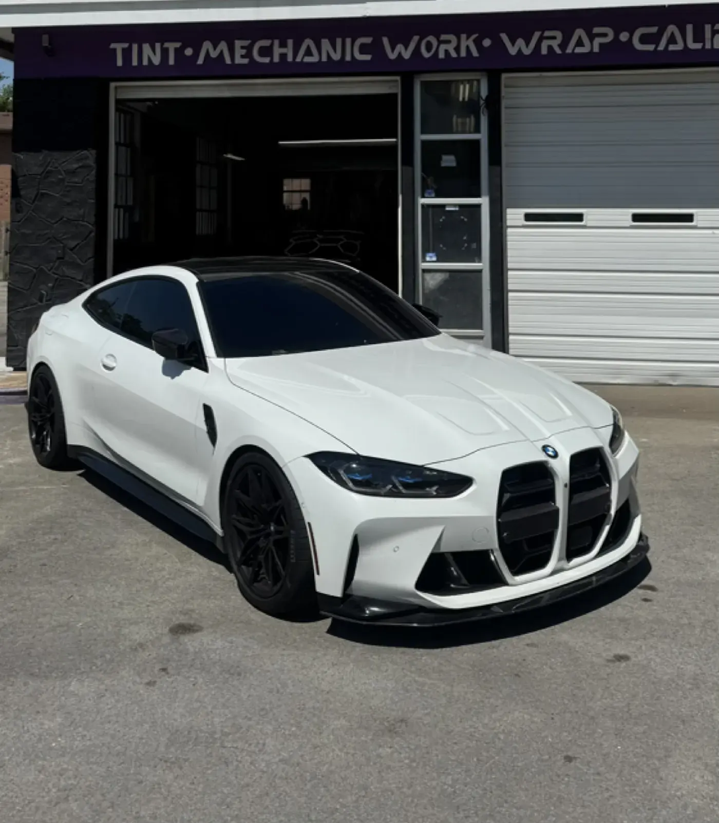 White BMW M4 with cosmetic upgrades in front of the shop