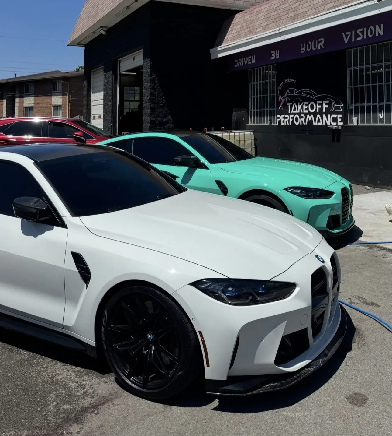 White and mint BMW M4s in front of the shop