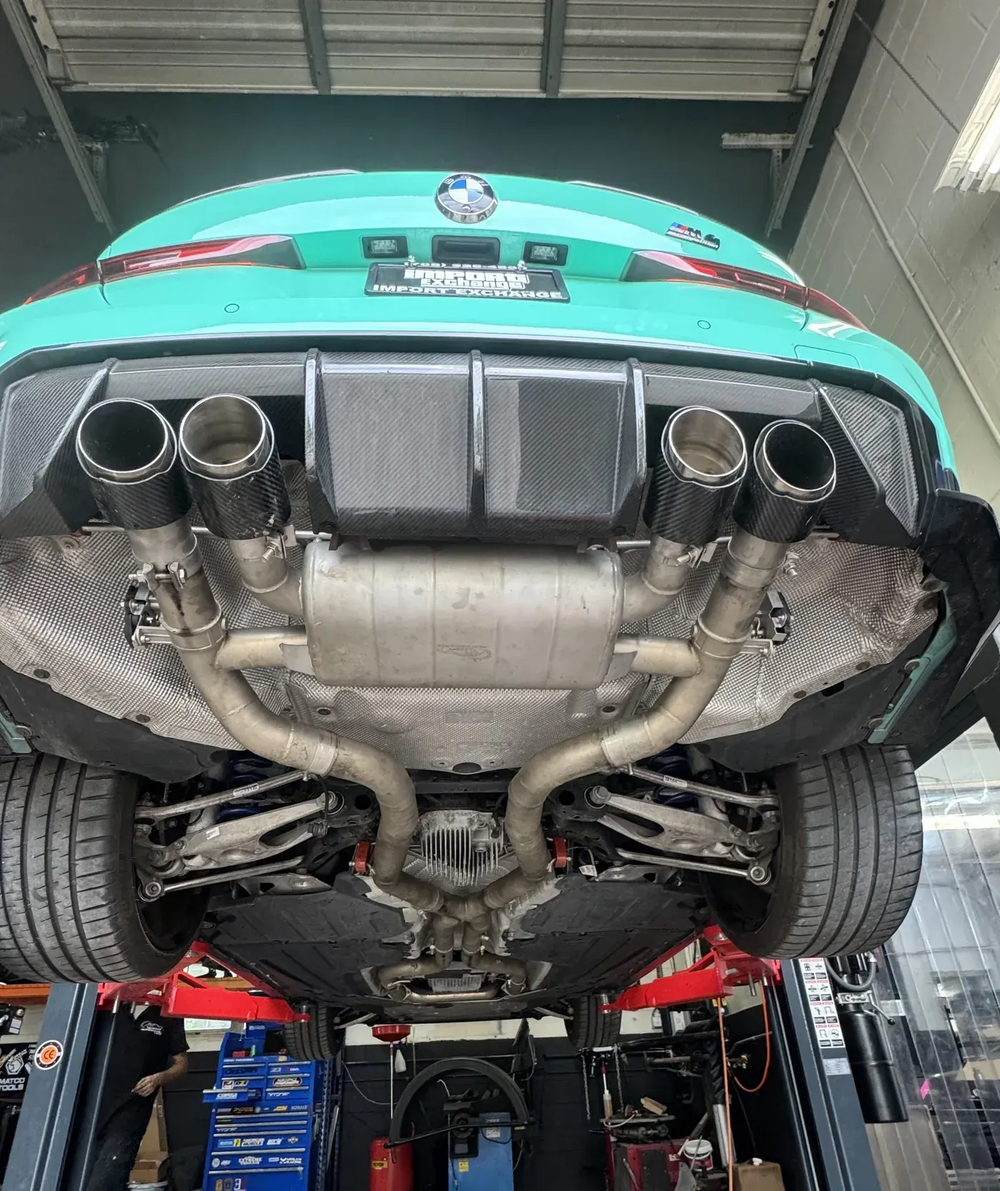 Quad-tip exhaust under a mint BMW M4 on the lift