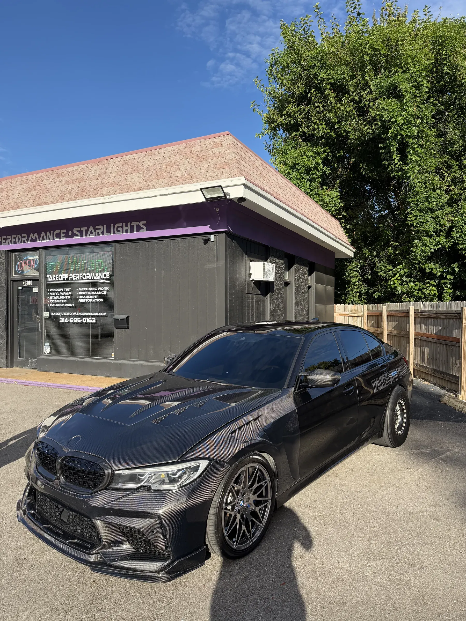 Black BMW M340i with a carbon hood in front of the Takeoff shop