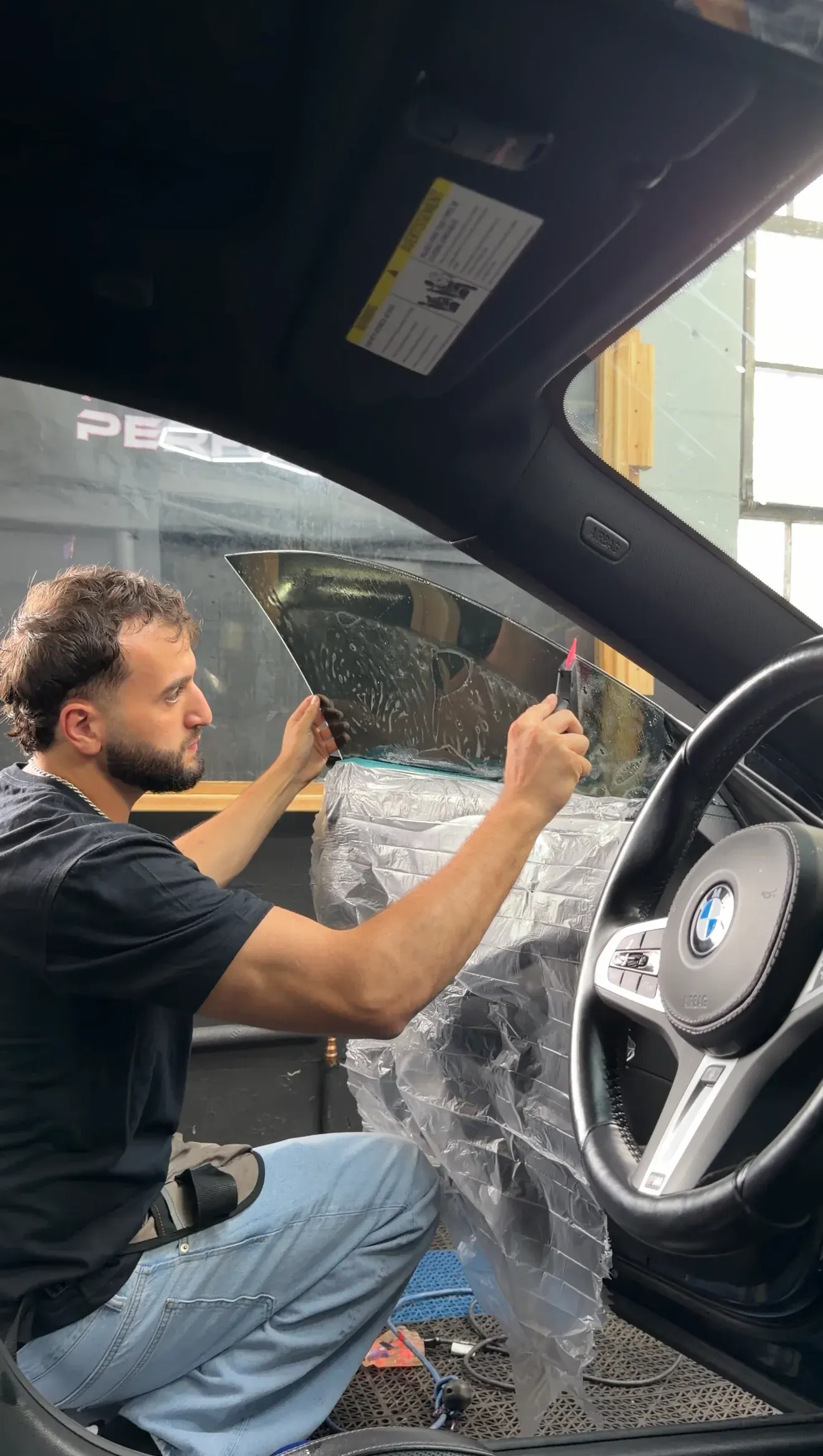 Technician fitting window tint from inside a car