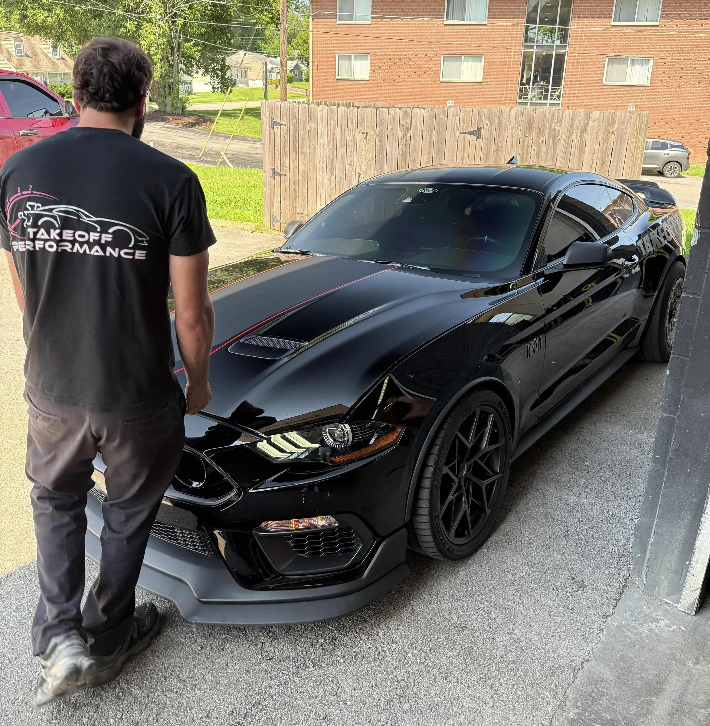 Technician in a Takeoff shirt beside a black Mustang